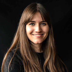 A professional portrait of a smiling woman with long hair in front of a black background.