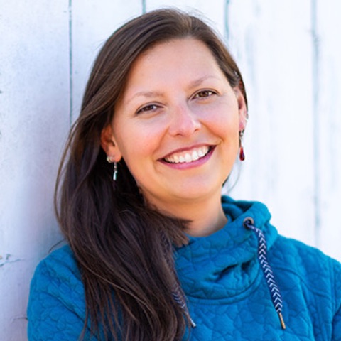 A smiling light-skinned woman with long dark hair wearing a comfy-looking blue top.