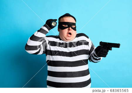 puzzled plump thief holding a gun on a blue background 68365565