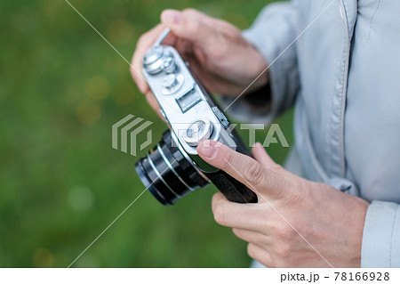 Female hands holding retro photo camera and push winding lever on background grass. 78166928