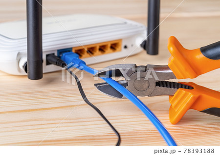 Wire snippers cutting the blue network cable connected to white Wi-Fi wireless router. 78393188