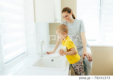 Happy mom teaches little son to wash dishes in the sink. 79241373