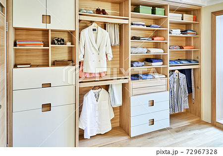 Modern wardrobe with clothes hanging on slide out racks and folded on the shelves. Modern furniture 72967328