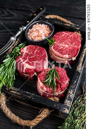 Fillet Mignon tenderloin raw meat veak steaks in wooden tray with herbs. Black wooden background. Top view 84765320