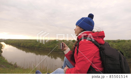 The girl drinks tea from a mug sitting on a high mountain and enjoying nature in the park. Woman traveler looking for adventure. Relax on the hike. Long distance hiking trips. Human explorer of 85501514