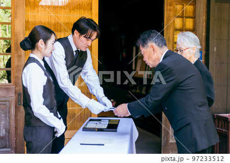 お葬式・告別式・お通夜の受付で香典を渡す高齢者の遺族・弔問客と葬祭ディレクター 97233512