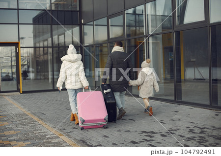 Family of three going on vacation. Man, woman and girl with a luggage going to airport terminal. Mother, father and daughter wearing warm clothes. 104792491