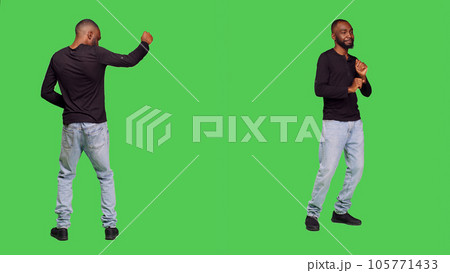 Joyful smiling man doing dance moves acting funny standing over full body green screen backdrop. Young adult being silly and dancing, feeling funky on camera. Leisure activity. 105771433