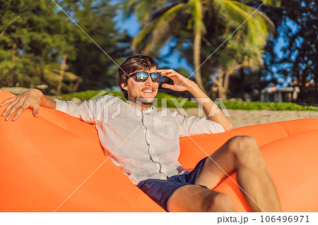 Summer lifestyle portrait of man sitting on the orange inflatable sofa on the beach of tropical island. Relaxing and enjoying life on air bed 106496971