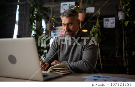 Focused caucasian man wearing stylish casual shirt using pc computer for work sitting in the modern office space 107221253