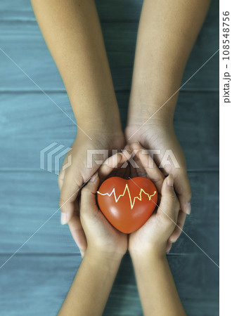 A hand holding red heart with heart wave.She is hand holding it on blue background.heart health,happy volunteer charity,The photo shows the principle of caring and good health. 108548756