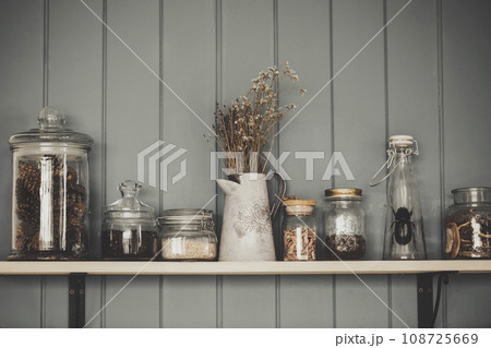 Witches kitchen. Shelf with vintage various glass jars and dry herbs, close-up, cinematic style. 108725669