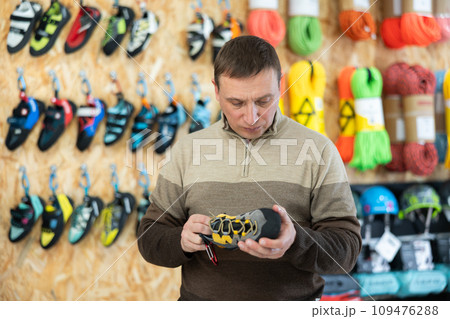 Man meticulously chooses climbing shoes in sports store 109476288