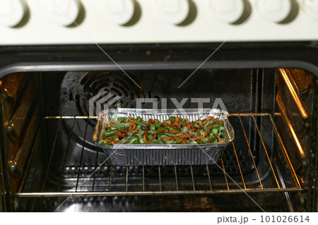 green bean casserole sprinkled with crispy fried onions in a aluminum food box in the oven, selective focus. 101026614