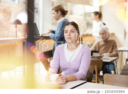 Portrait of focused young female freelancer surfing Internet on notebook while drinking tea or coffee in cafeteria 101034364