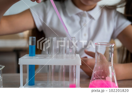 A schoolgirl conducts experiments in a chemistry lesson. Girl pouring colored liquids from a beaker.  102201820