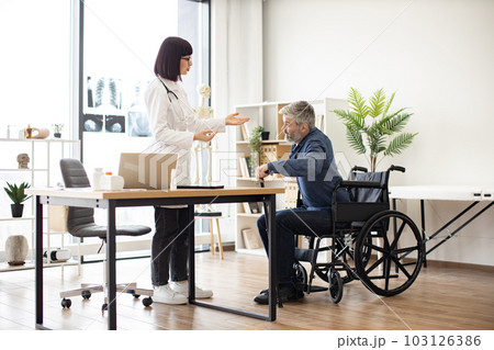 Therapist helping man with cane to stand from wheelchair 103126386