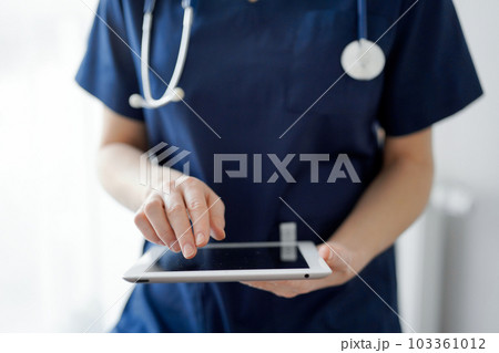 Doctor woman using tablet computer while standing near panorama window in clinic, close up. Physician or surgeon at work. Medicine concept 103361012