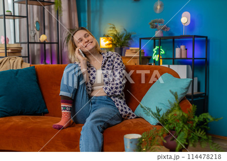 Happy young Caucasian woman making mobile phone conversation with friends sitting on couch at home 114478218