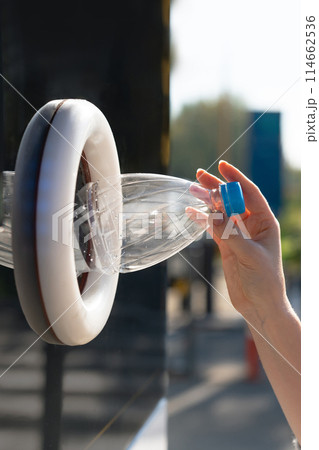 Woman uses a self service machine to receive used plastic bottles and cans on a city street.. 114662536