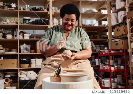 Candid portrait of smiling Black senior woman enjoying pottery class in art studio lit by sunlight copy space 115316439