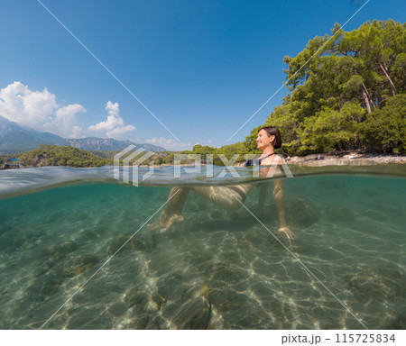 Young female on holidays enjoy floating on a crystal clear water beach of Antalya Turkey. Asian beautiful woman swimming with open arms. Relax and tranquility. Travel and Holiday concept. 115725834