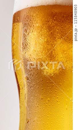 Close-up photo of cold, golden, lager alcohol drink, beer with thick white foam against grey studio background. 115848903