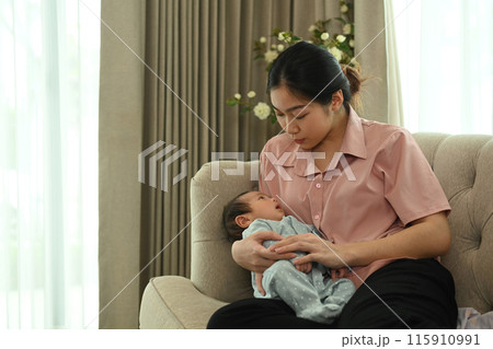 Asian young mother sitting on a sofa and holding a newborn baby in her arms. Motherhood concept 115910991