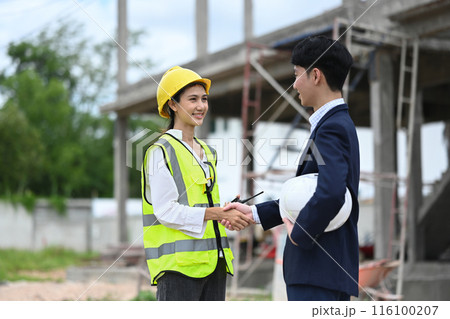 Handsome businessman in black suit and engineer shaking hands on construction site 116100207