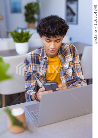 Using smartphone and laptop, teenage boy working from home at table 116314849