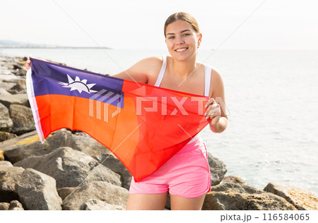 Enjoying vacation in Taiwan. Young woman with national Taiwanese flag on the seashore on sunny day 116584065