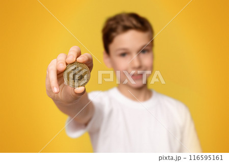 Cryptocurrency and modern finance. Cheerful boy holding golden bitcoin, orange studio background 116595161