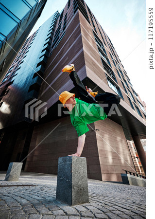 dynamic photo of man flips upside down, dressed fashion clothes popping against background of modern urban architecture. 117195559