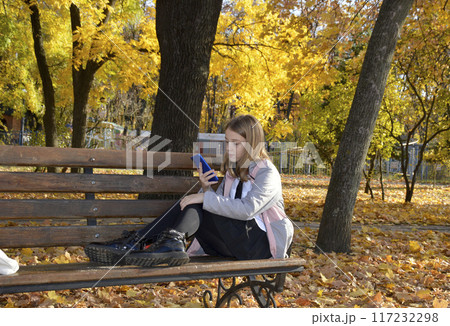 girl with a phone in her hands on a bench in an autumn park 117232298