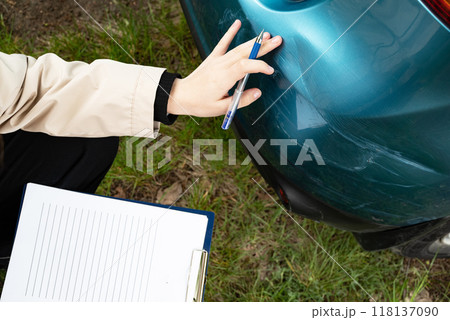 A close-up of a damaged car bumper with a person filling out a form on a tablet, getting insurance. 118137090