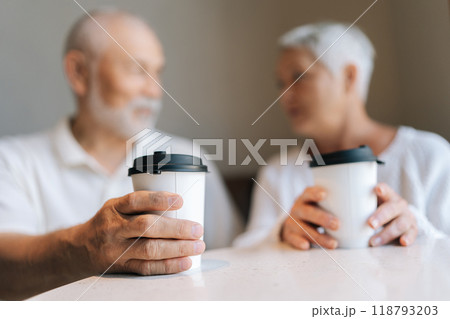 Selective focus shot of elderly couple spending quality time together, holding takeaway coffee cups while engaging in conversation at cozy cafe, loving looking at each other. Concept of active aging. 118793203