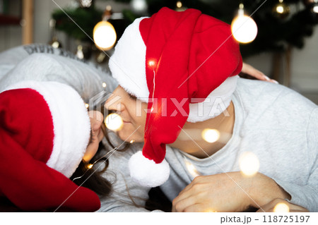 Young beautiful men women Santa hats looking each other tenderly near Christmas tree for New Year 118725197