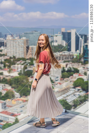 Female tourist or businesswoman standing on a skyscraper rooftop with a panoramic view of Mexico City. Travel or international business in Mexico concept 118986130