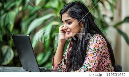 Young Indian woman smiling while working on laptop in a green indoor setting 119531632