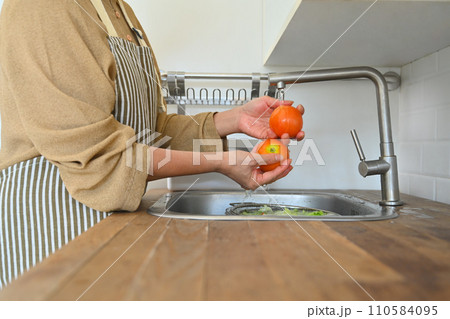 Cropped shot senior housewife in apron washing fresh vegetables for salad in kitchen 110584095