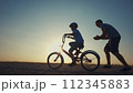 family play in the park. father teaching son to ride a bike. happy family kid dream concept. son learn to ride a bike silhouette. father supporting sunset child son riding bike summer in the park 112345883