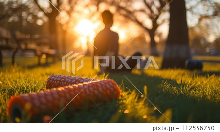 Man relaxing on grass with fitness equipment in a sunny park 112556750