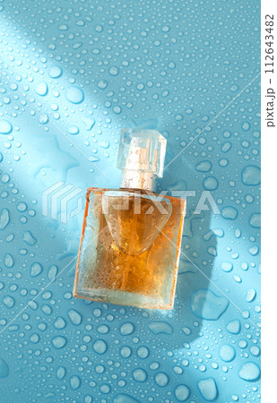 Perfume woman bottle on blue background with hard light and water drops. with shadows flat lay, top view 112643482