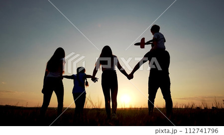 family walks across the field. happy childhood concept for little child. big happy family walks across the field on the grass holding hands, sunset on the background, silhouettes lifestyle 112741796