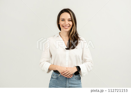 A confident young woman with long brown hair wearing a casual white blouse and blue jeans 112721153