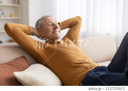 Relaxed elderly man reclining on couch at home 112725021