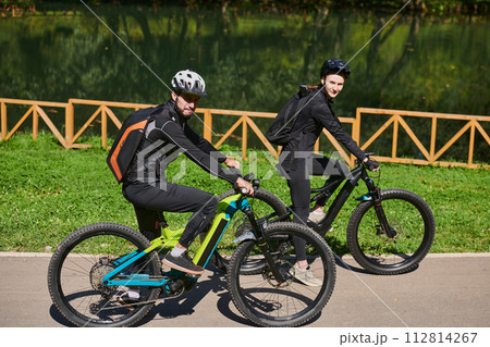 A blissful couple, adorned in professional cycling gear, enjoys a romantic bicycle ride through a park, surrounded by modern natural attractions, radiating love and happiness 112814267