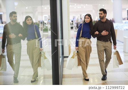 Full length portrait of young couple enjoying shopping together in mall with window display reflection, copy space 112999722