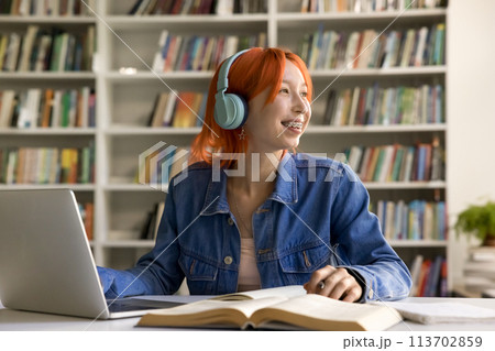 Red-head student girl listen audio course studying on-line in library 113702859