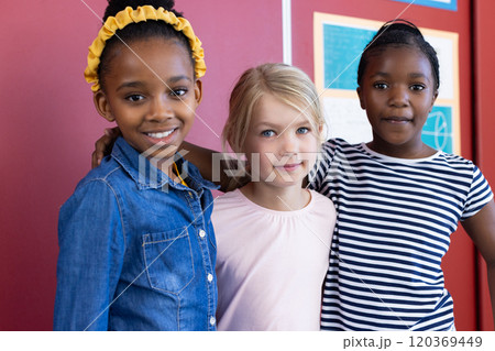 Standing together and smiling, multiracial schoolgirls posing for photo in classroom 120369449